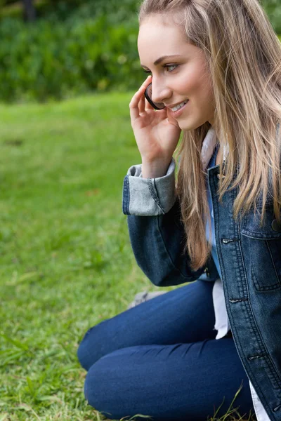 Joven chica sonriente hablando por teléfono mientras se sienta en el gra —  Fotos de Stock