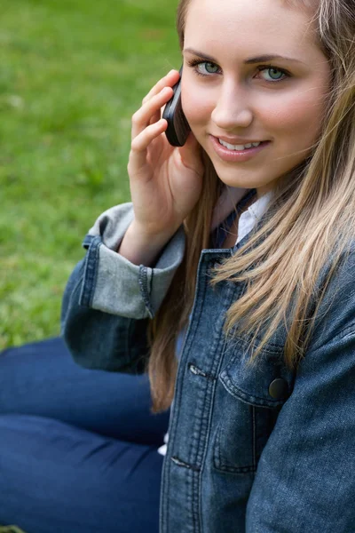 Young smiling girl talking on the phone while sitting down in a — Stock Photo, Image