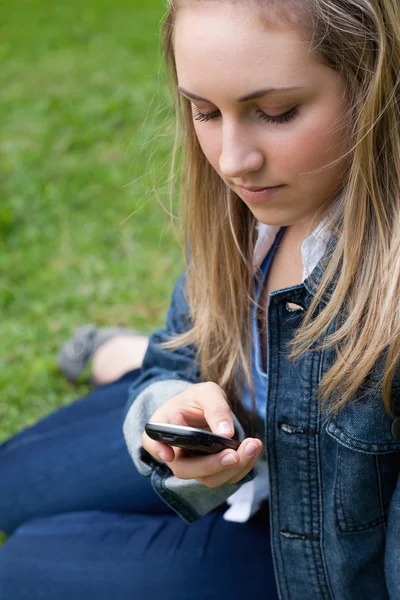 Молодая девушка отправляет сообщение, сидя на траве — стоковое фото
