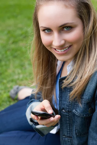 Joven chica rubia sentada en la hierba mientras envía un mensaje de texto —  Fotos de Stock