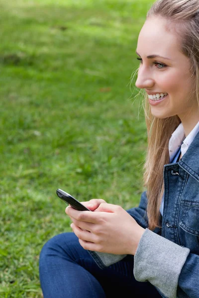 Junge lächelnde Frau sendet einen Text, während sie in einem Park sitzt — Stockfoto