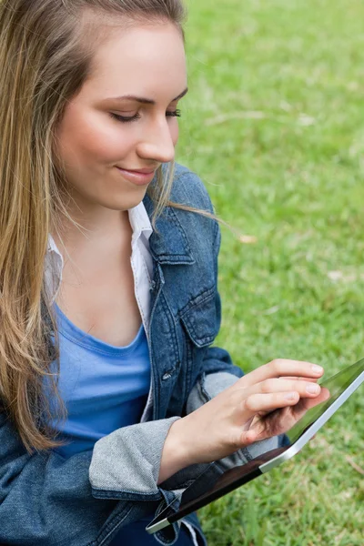 Молодая мирная женщина, использующая свой планшетный компьютер, сидя на гр — стоковое фото