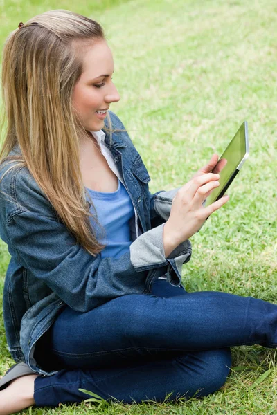 Joven chica rubia atractiva sentada en la hierba mientras lo usa —  Fotos de Stock