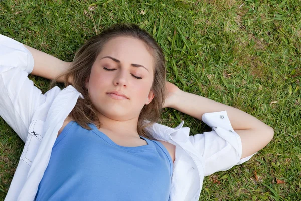 Joven chica relajada durmiendo en la hierba mientras coloca sus manos — Foto de Stock