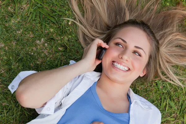 Joven mujer sonriente acostada boca arriba mientras usa su teléfono celular — Foto de Stock