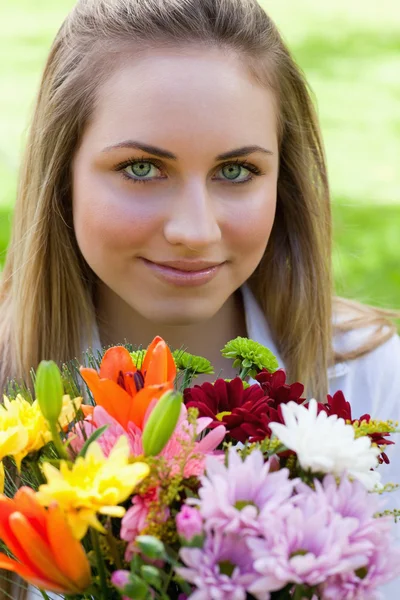 Jovem menina relaxada segurando um monte de flores em um jardim público — Fotografia de Stock