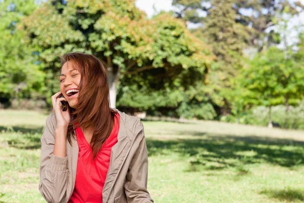 Jovem mulher entusiasticamente rindo enquanto no telefone em um o — Fotografia de Stock