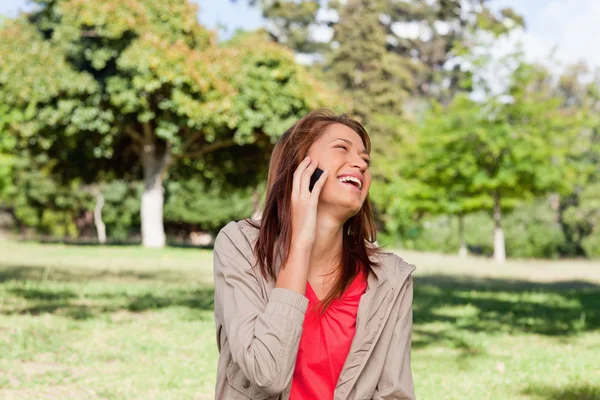 Femme riant joyeusement sur un téléphone tout en se tenant dans une mamie ensoleillée — Photo