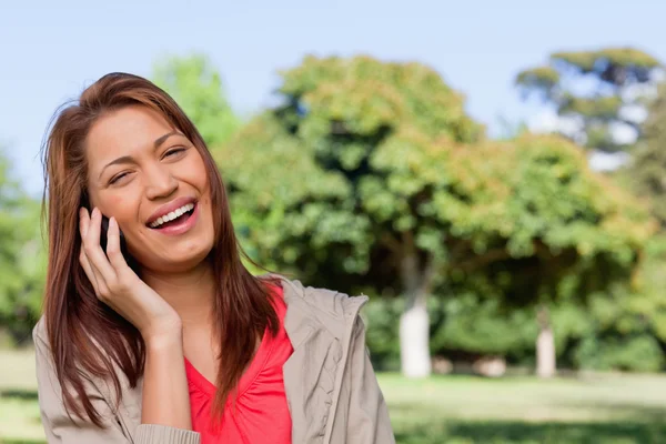 Młoda kobieta śmiejąc się szczęśliwie na telefon w parku jasny — Zdjęcie stockowe