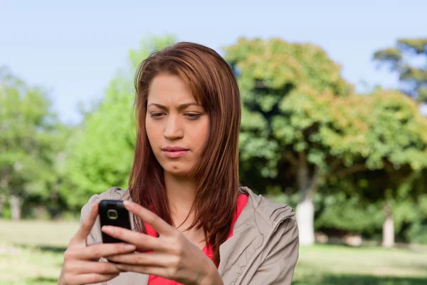 Ernstige vrouw een SMS-bericht op een heldere grasland gebied lezen — Stockfoto