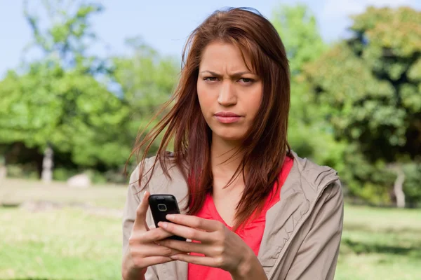 Kobieta z rufy wyrażenie na jej twarzy trzymając telefon — Zdjęcie stockowe