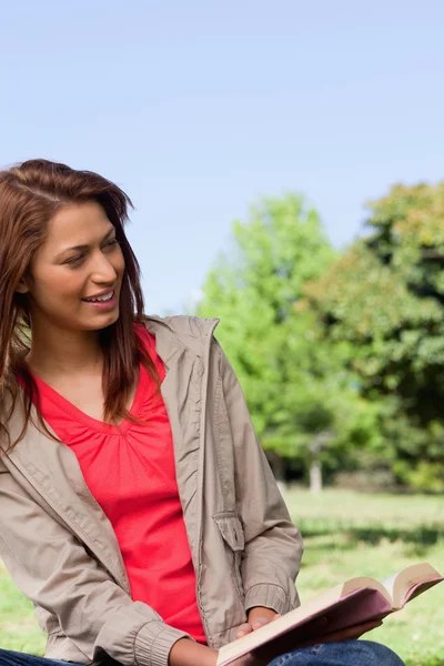 Vrouw leest een boek terwijl zitten in een heldere park — Stockfoto