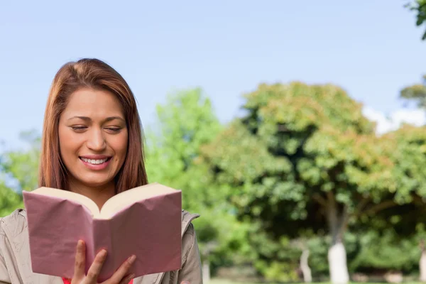 Jovem mulher feliz lendo um livro em um parque ensolarado — Fotografia de Stock