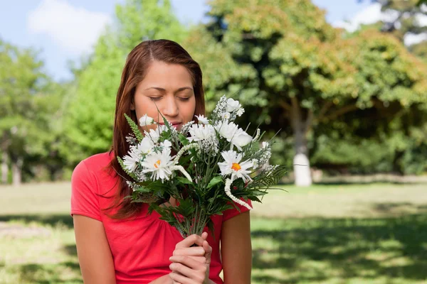 Vrouw ruiken een bos van bloemen terwijl je in een park — Stockfoto
