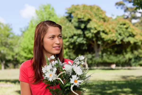 Junge Frau schaut zur Seite, während sie einen Strauß Blumen in der Hand hält — Stockfoto