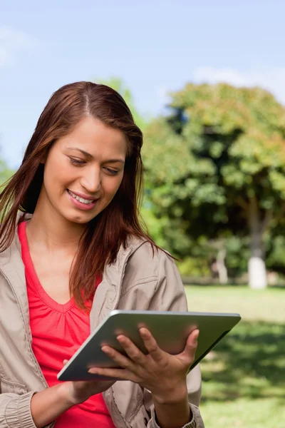 Young woman using a tablet while standing in bright park — Stock Photo, Image