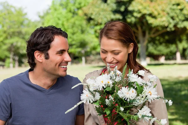 Frau schaut glücklich in einen Blumenstrauß, während sie beobachtet wird — Stockfoto