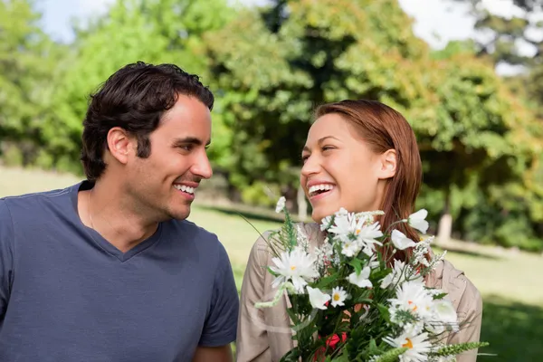 Mann sieht seinem Freund beim Lachen zu, während er einen Blumenstrauß in der Hand hält — Stockfoto