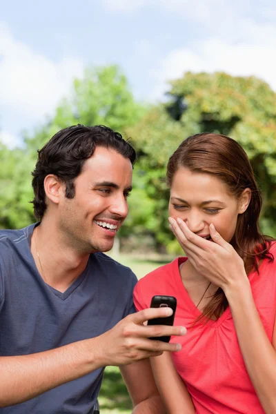 Mujer riéndose de algo que se le muestra en el ph de su amigo —  Fotos de Stock