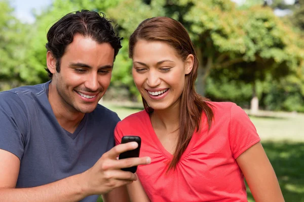 Dos amigos sonriendo mientras miran algo en un móvil — Foto de Stock