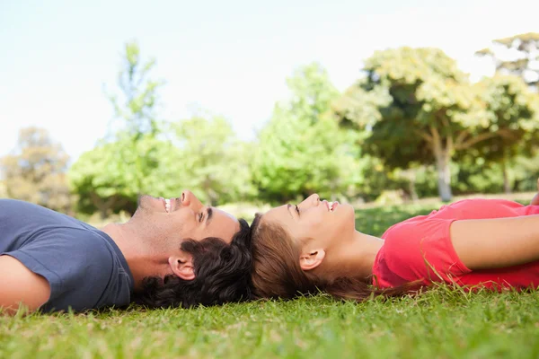 Two smiling friends looking upwards while lying head to head — Stock Photo, Image