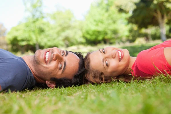 Two smiling friends looking towards the side while lying head to — Stock Photo, Image