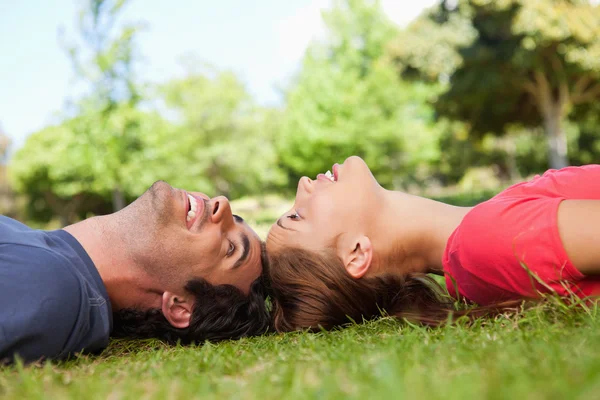Two smiling friends looking at each other while lying head to he — Stock Photo, Image