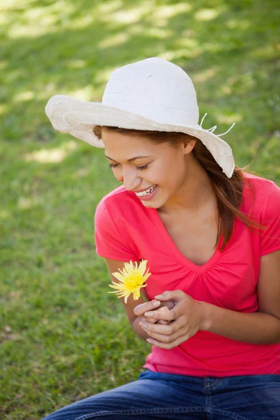 Donna ridendo mentre indossa un cappello bianco e tenendo un fl giallo — Foto Stock