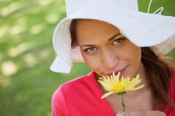 Donna che indossa un cappello bianco mentre annusa un fiore giallo — Foto Stock
