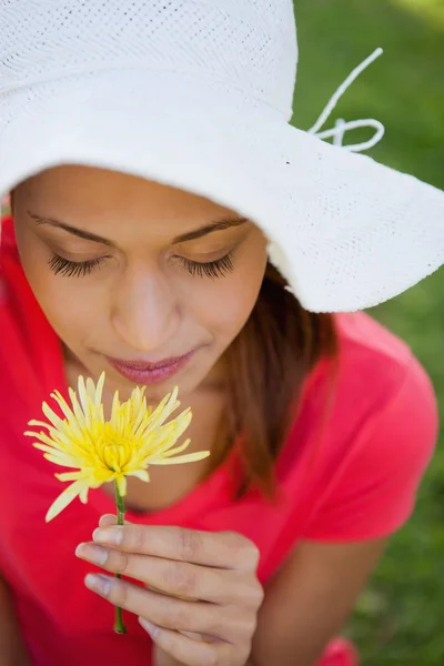 Mujer con un sombrero blanco mientras huele una flor mientras mira — Foto de Stock