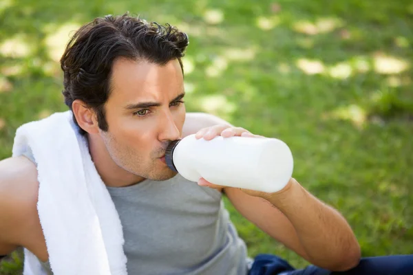 Άνθρωπος με μια πετσέτα στον ώμο του, πίνει νερό από ένα μπουκάλι σπορ — Φωτογραφία Αρχείου