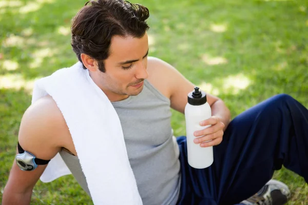 Hombre con una toalla en el hombro mirando una botella deportiva — Foto de Stock