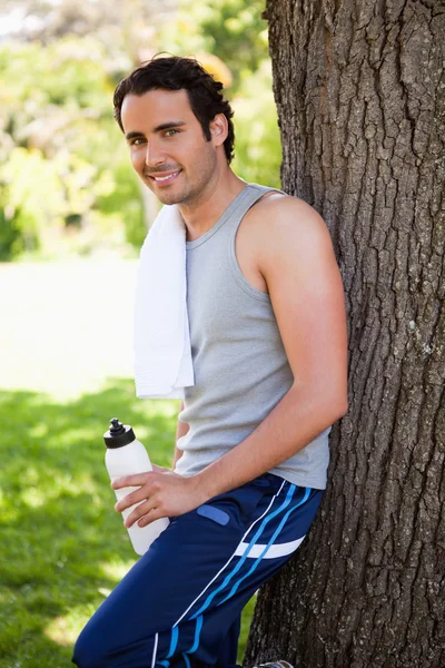 Sonriente hombre mirando a un lado mientras sostiene una botella de deporte un — Foto de Stock