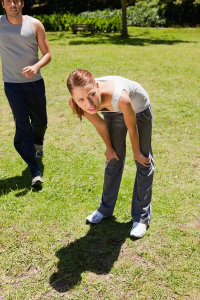 Frau bückt sich, während ein Mann hinter ihr joggt — Stockfoto