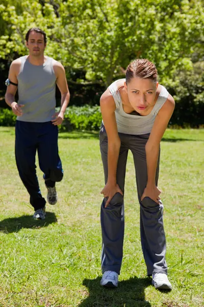 Woman bending over while a man is jogging in the background — Stock Photo, Image