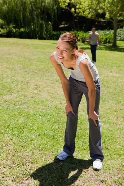 stock image Woman bending over while man is walking in the background