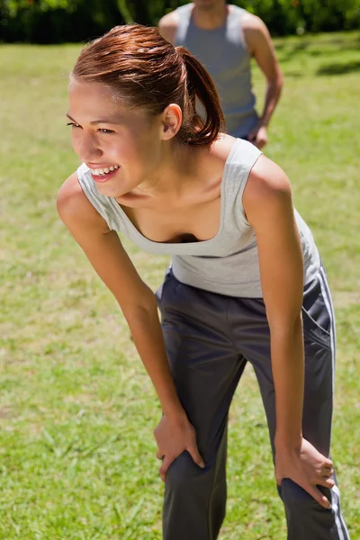 Smiling woman bending over while a man is walkng behind her — Stock Photo, Image