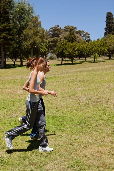 Two friends jogging along side each other across grass — Stock Photo, Image