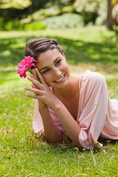 Woman lying on her front while holding a flower against her head — Stock Photo, Image
