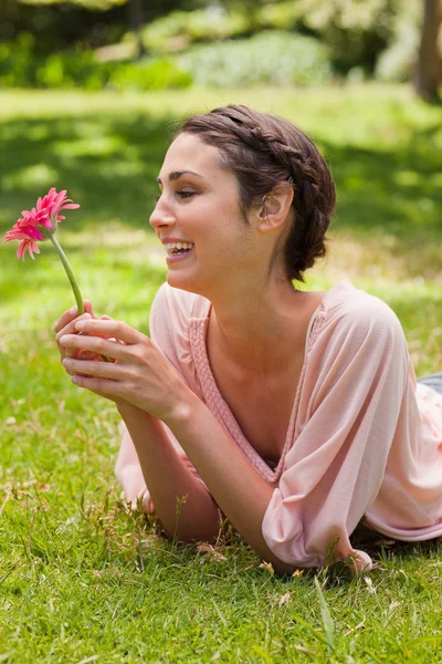 Mujer acostada en su frente riendo mientras mira una flor — Foto de Stock