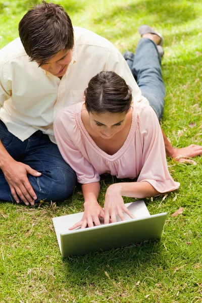 Two friends looking into a laptop together while lying down — Stock Photo, Image