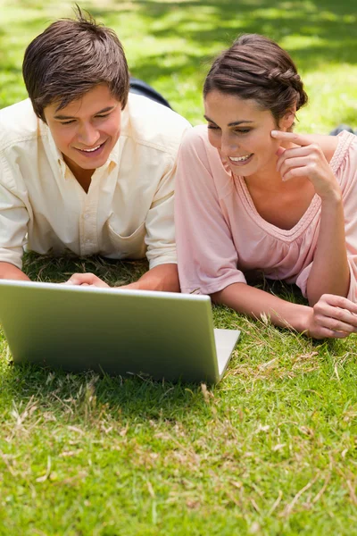 Two friends using a laptop together while lying down — Stock Photo, Image