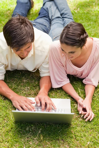 Two friends looking at something on a laptop while lying down — Stock Photo, Image