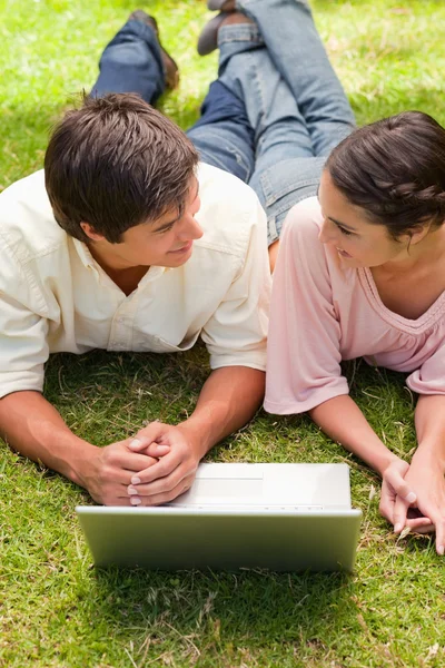 Two friends looking at each other as they lie down with a laptop — Stock Photo, Image