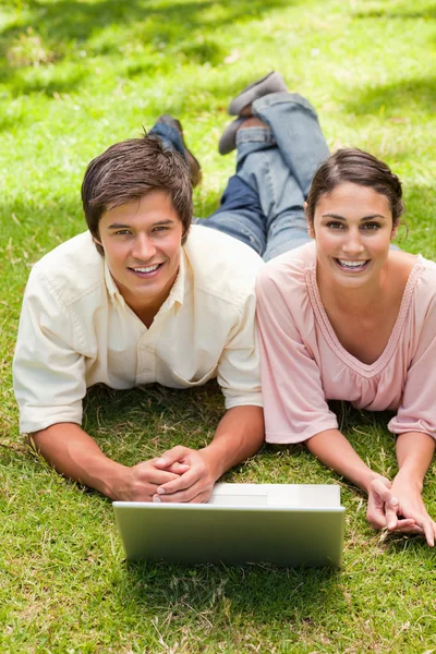 Two friends laughing while looking ahead as they use a laptop — Stock Photo, Image