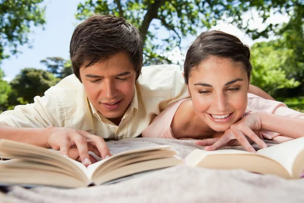 Dos amigos sonriendo mientras leen libros mientras se acuestan — Foto de Stock