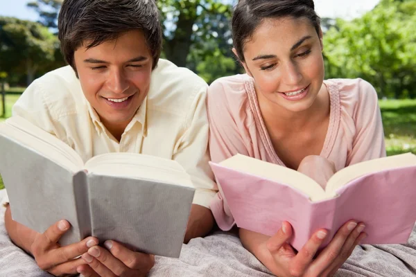 Twee vrienden glimlachen als ze lezen terwijl liggend op een deken — Stockfoto