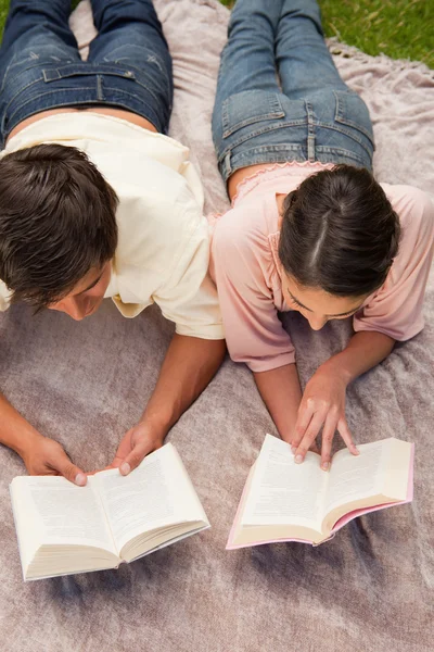 Man and a woman reading while lying on a blanket — Stock Photo, Image