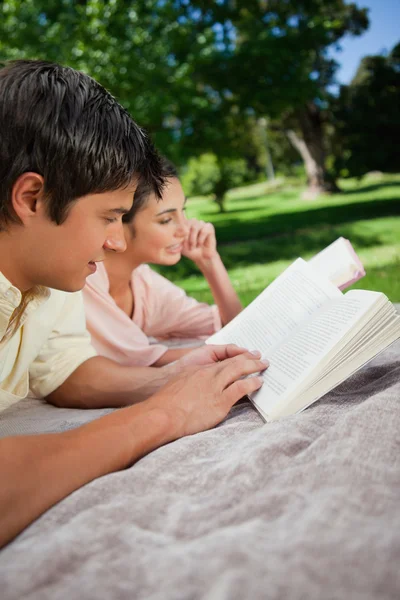 Dos amigos leyendo libros mientras yacen en un parque — Foto de Stock