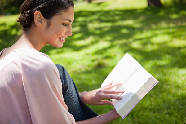 Mulher lendo um livro enquanto sentado na grama — Fotografia de Stock